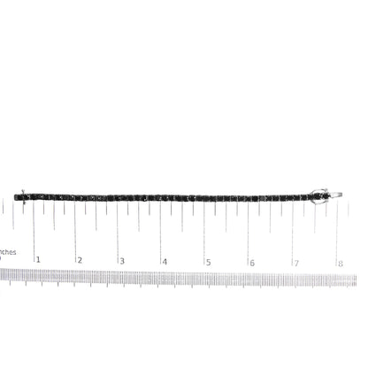 White metal bracelet with round black gemstones in prong settings, displayed flat on a ruler for size reference, shot from above.