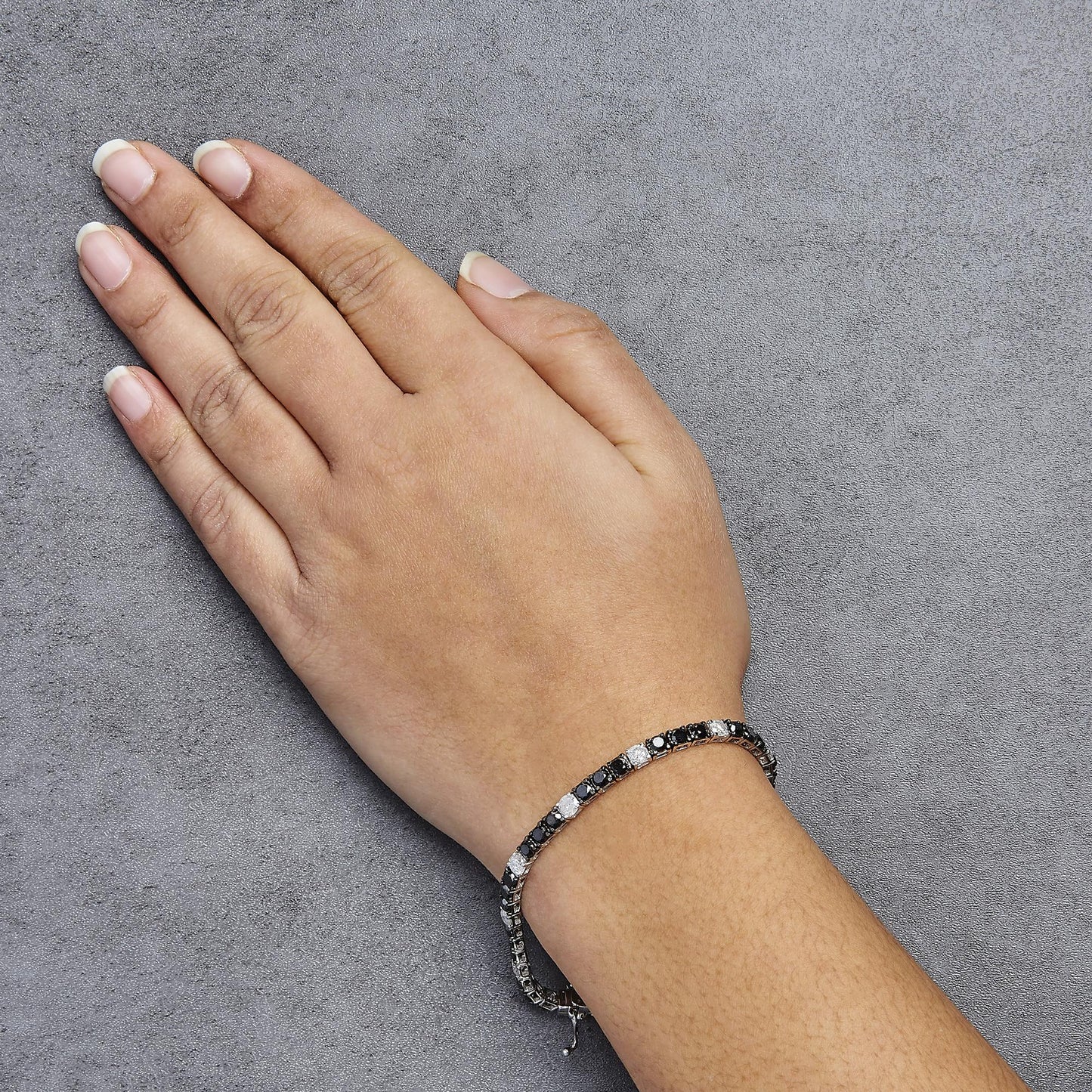 White metal bracelet with alternating black and white round gemstones in 4-prong settings, worn on a model's wrist, shot from above.