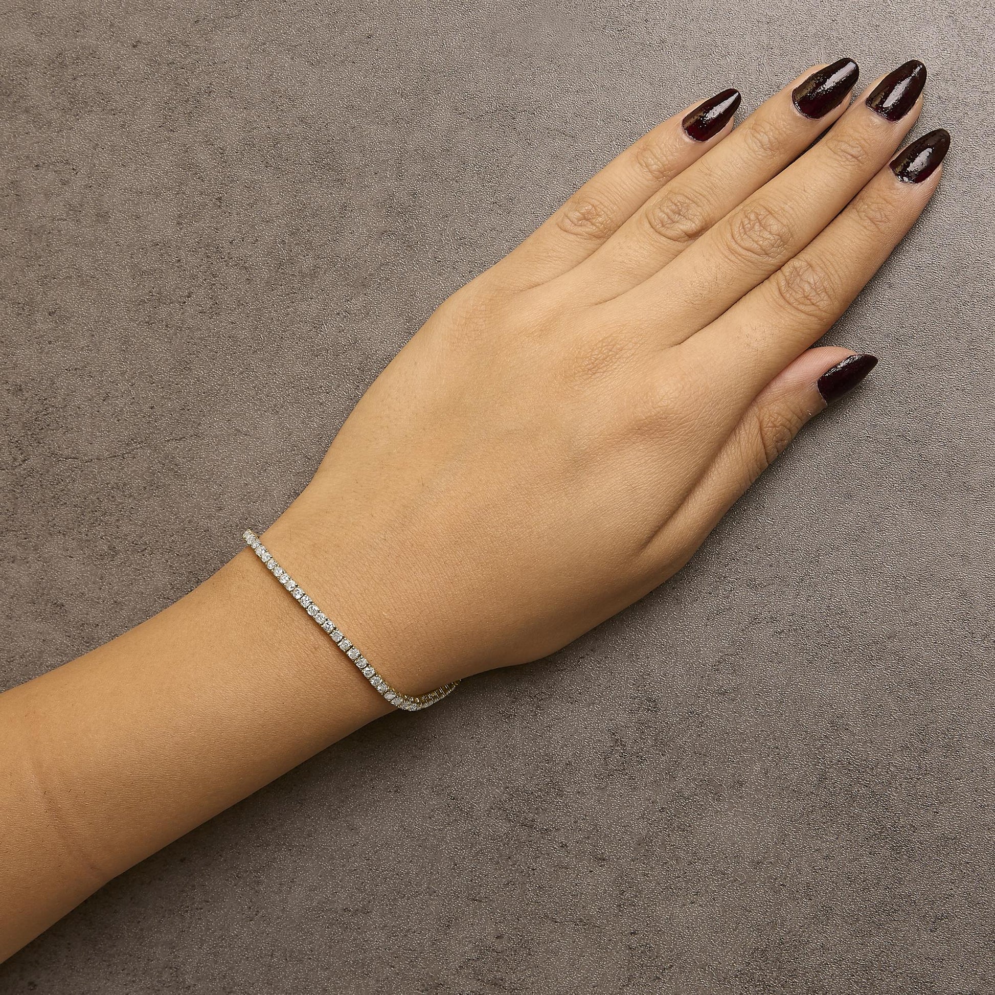 Yellow metal bracelet with round brownish gemstones in 4-prong settings, worn on a model's wrist, top-down angle.