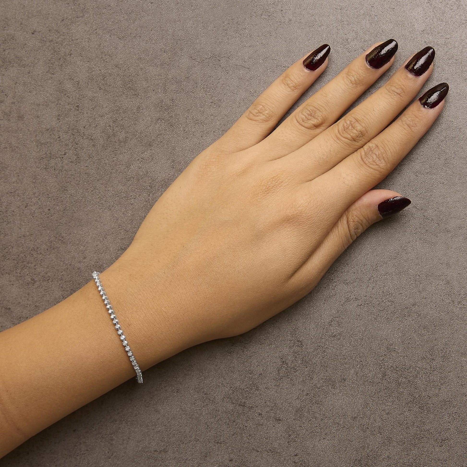 White metal bracelet with round white gemstones in prong settings, shown worn on model's wrist, top view angle.