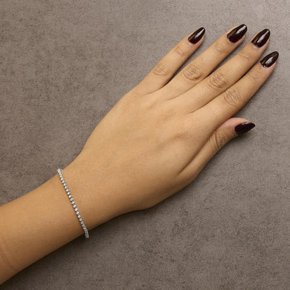 White metal bracelet with round white gemstones in prong settings, shown worn on model's wrist, top view angle.