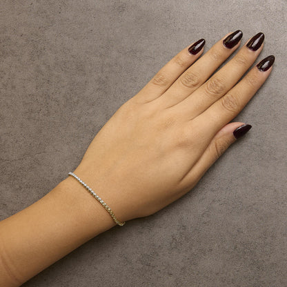 Close-up top view of a model's hand wearing a yellow metal bracelet featuring two rows of round white gemstones in prong settings.