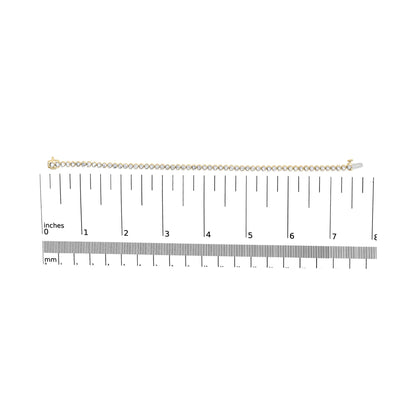 Yellow metal bracelet with two rows of round white gemstones in prong settings, shown horizontally from above on a scale.