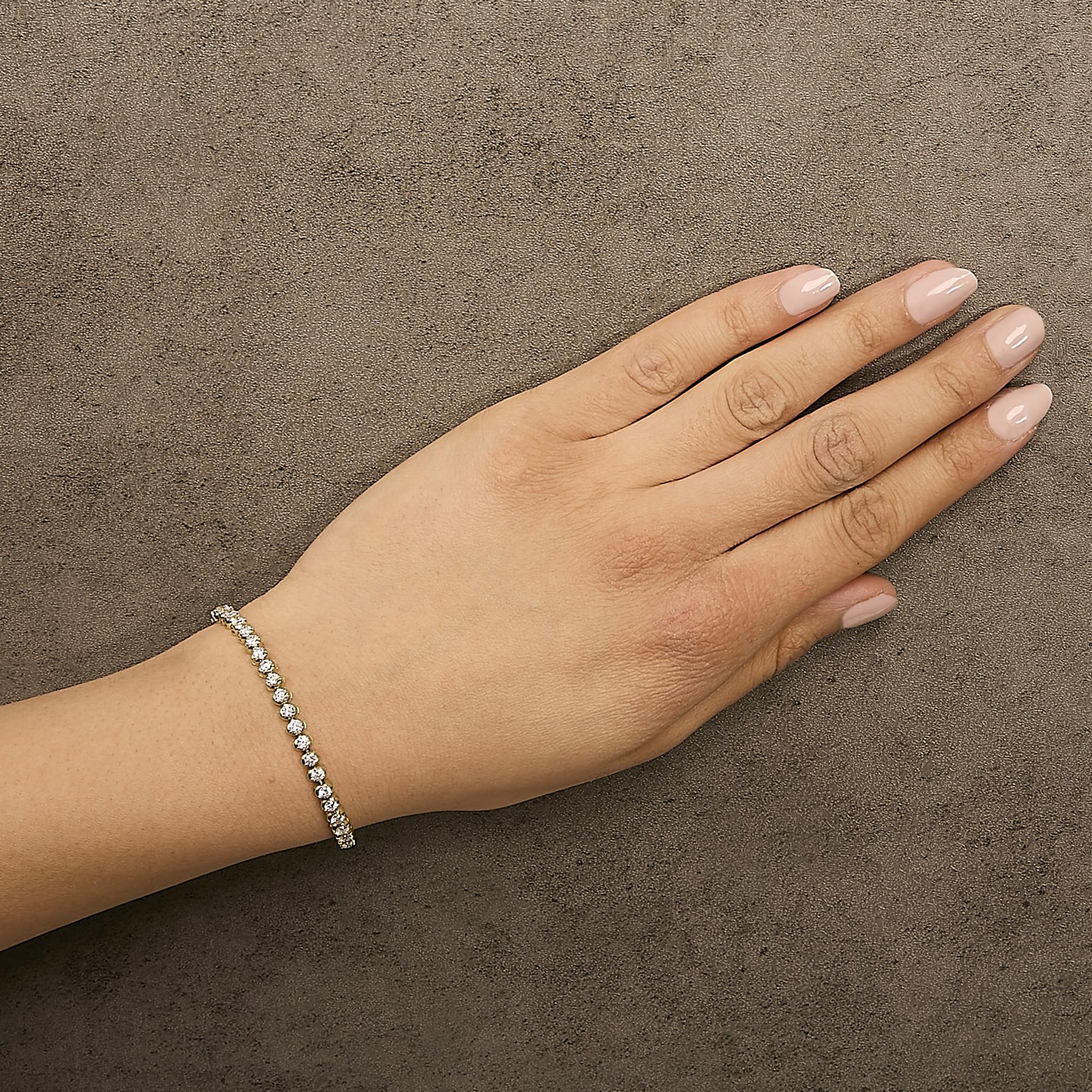 Yellow bracelet with white round gemstones in prong settings, shown worn on a model's wrist, angled top-down on a textured surface.