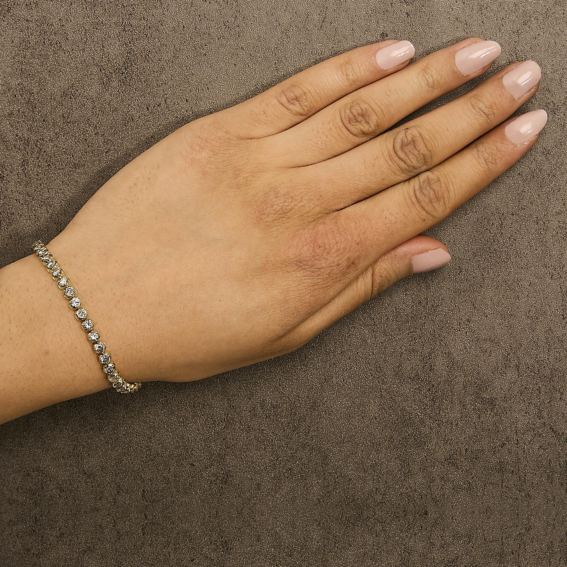 Close-up front angle of a model's hand wearing a yellow metal bracelet with round white gemstones in a prong setting.
