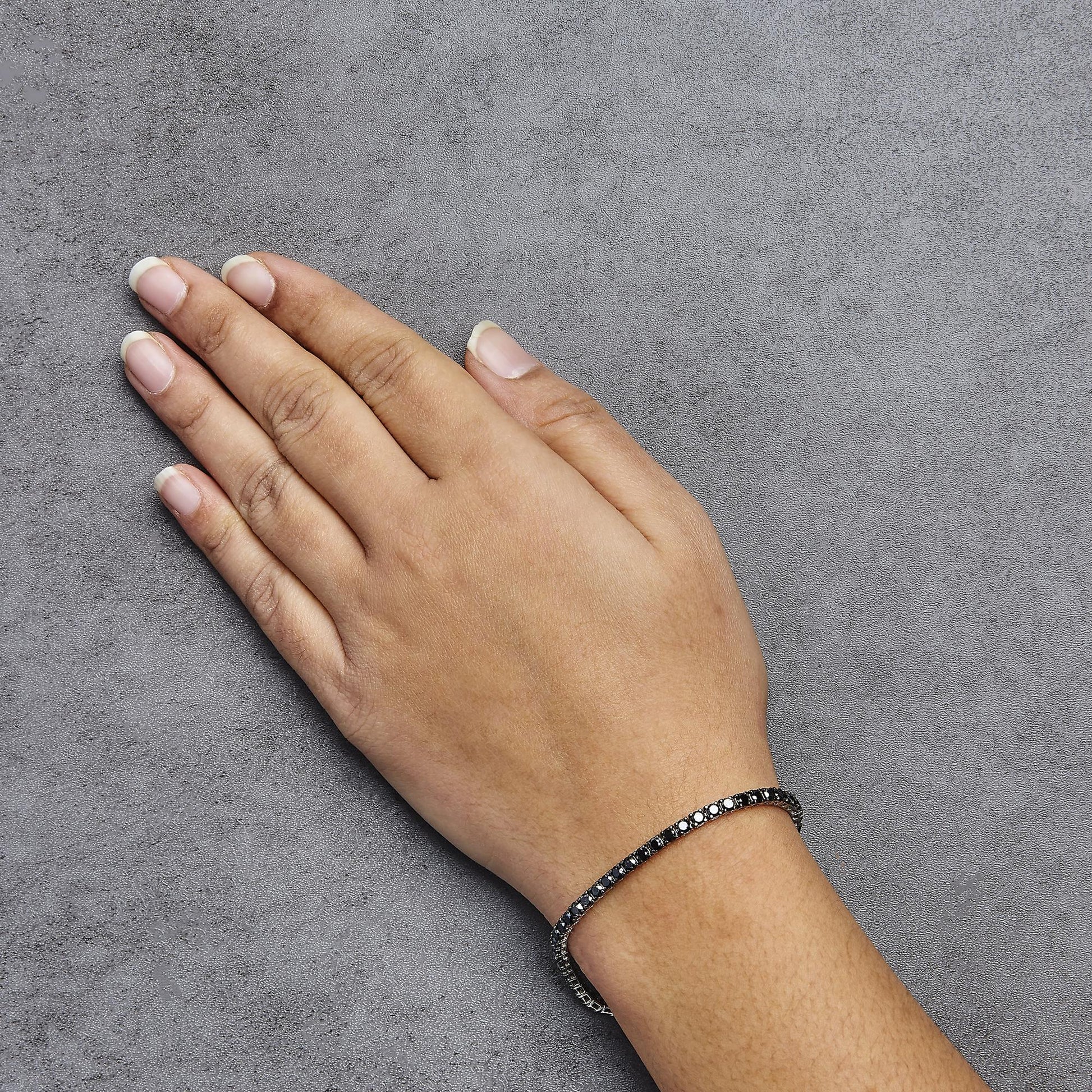 White metal bracelet with black round gemstones in prong setting, worn on a model’s wrist, top-down view.