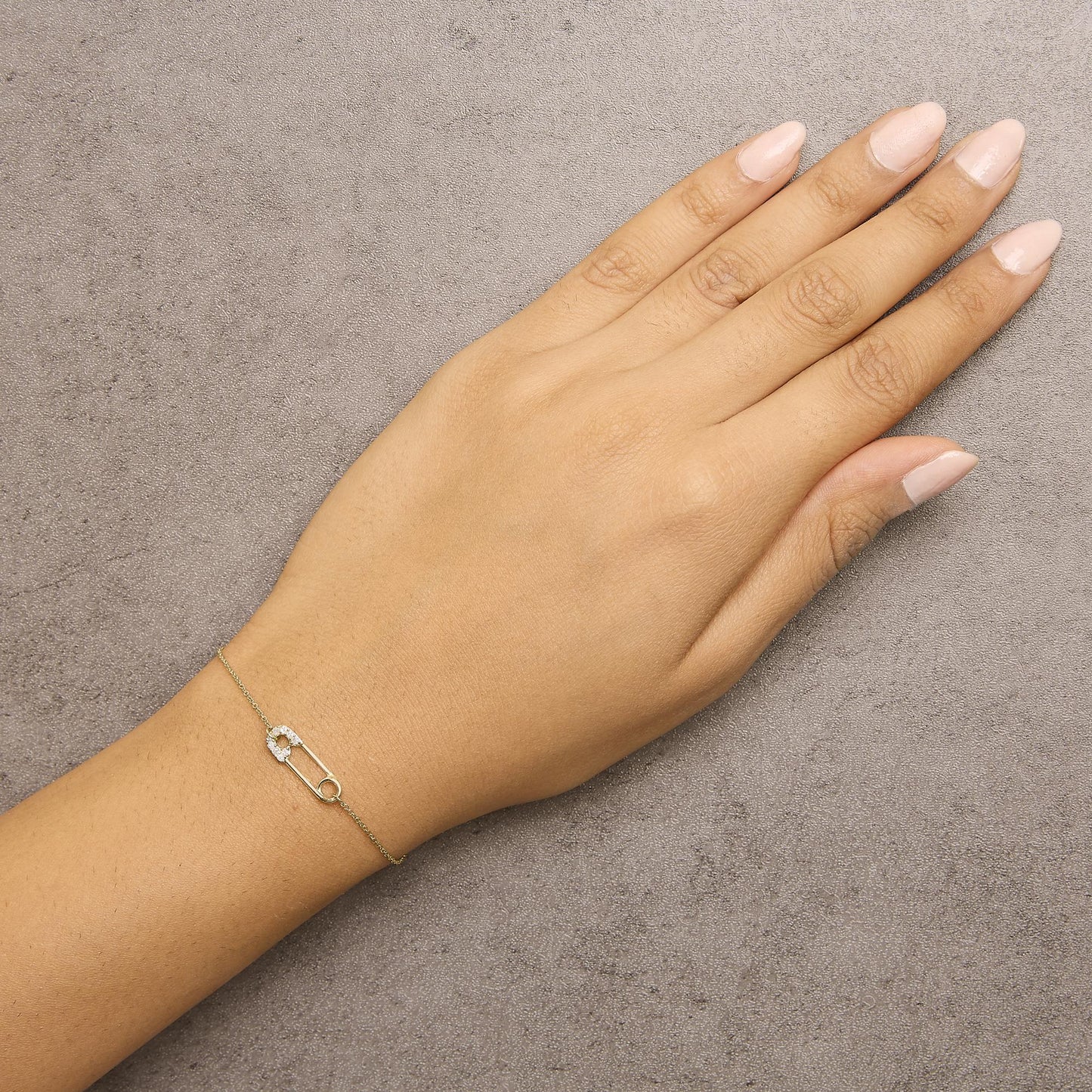 Yellow metal bracelet with a safety pin design featuring white round gemstones, shown worn on a model's wrist from a top-down angle.