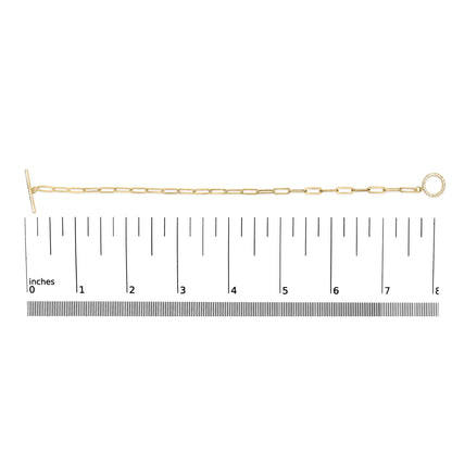 Top-down view of a yellow metal bracelet with elongated links, featuring a circular charm set with white round gemstones, displayed on a ruler for size reference.