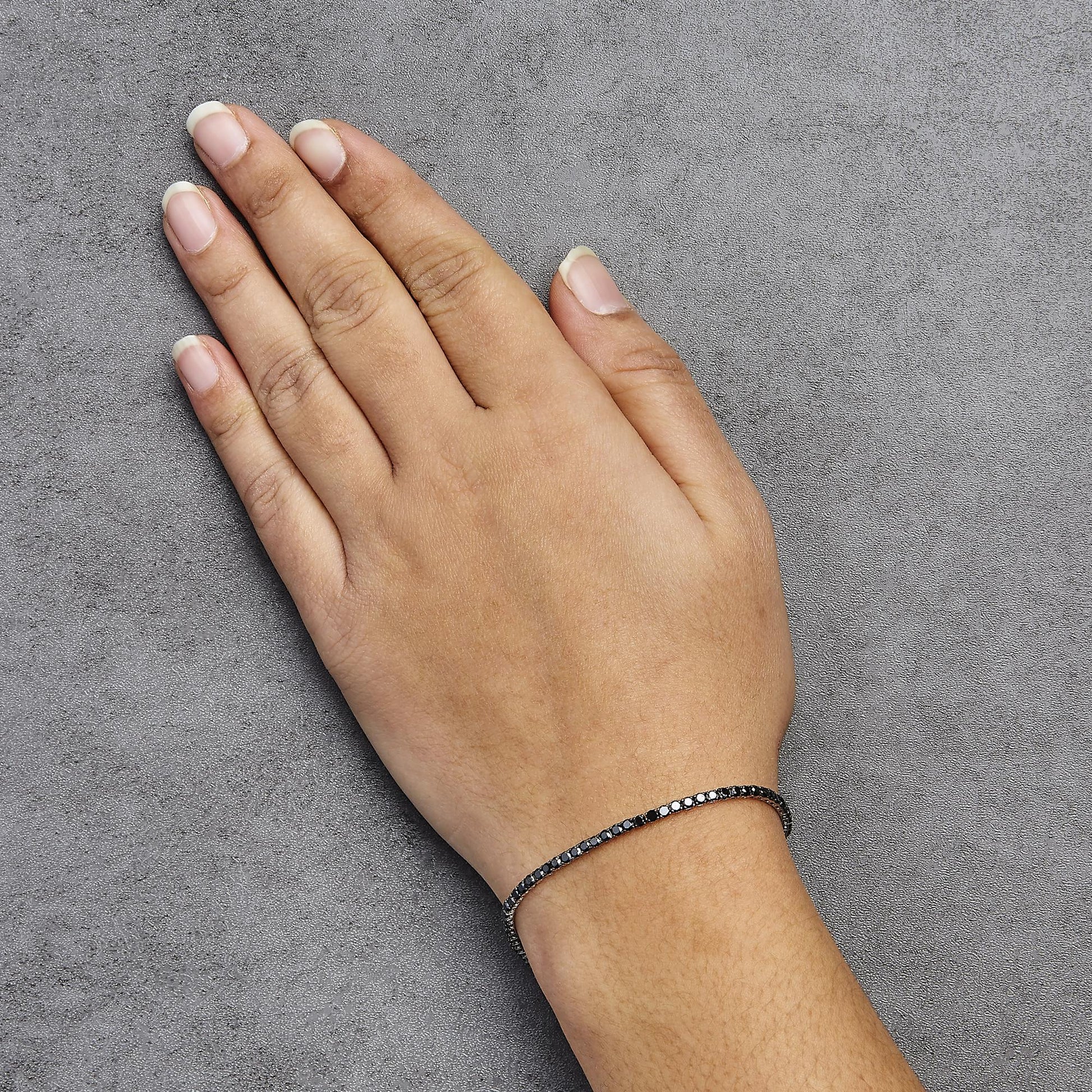 Close-up side angle of a white metal bracelet with round black gemstones in prong settings, worn on a model's wrist against a gray textured background.