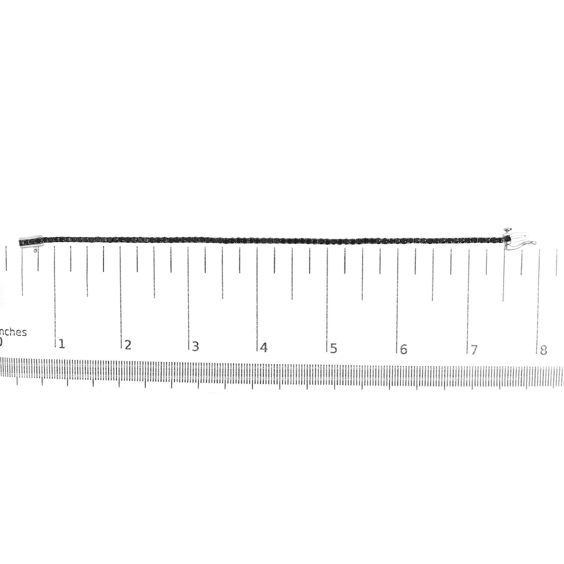 White metal bracelet with prong-set round black gemstones laid flat on a ruler for size reference, shown from a top-down angle.