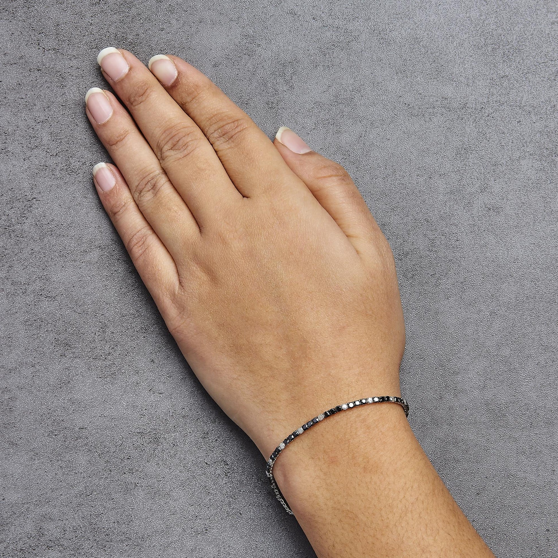 Close-up front view of a white metal bracelet with alternating black and white round gemstones in four-prong settings, worn on a model's wrist against a grey textured background.