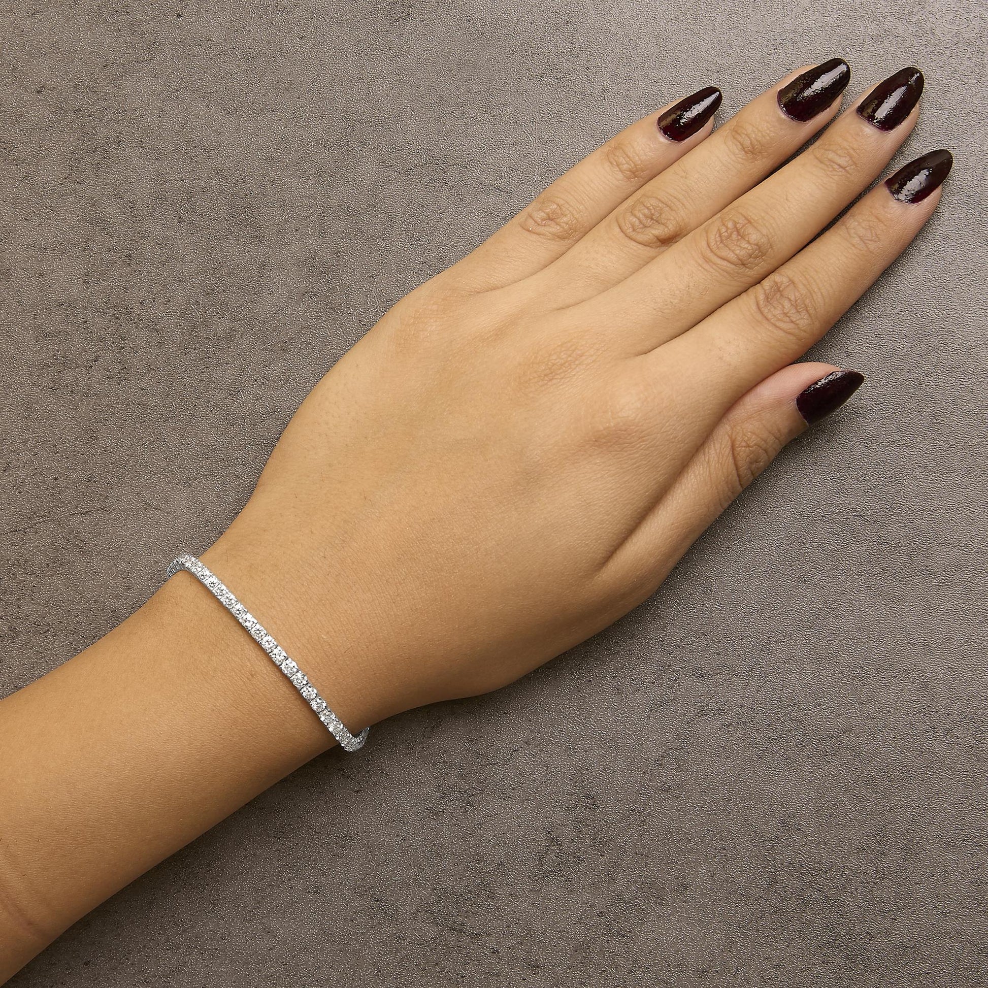 White metal bracelet with alternating sizes of round white gemstones in 4-prong settings, shown on model's wrist from above.