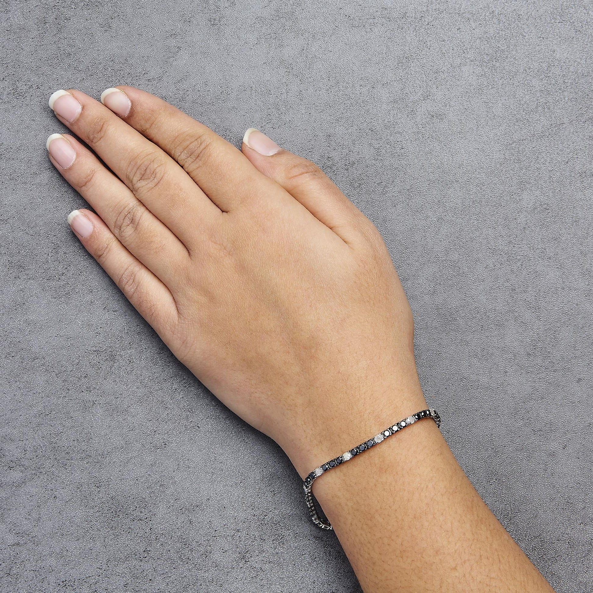 White metal bracelet with alternating black and white round gemstones in 4-prong settings, worn on a model's wrist, shown from above at an angle.