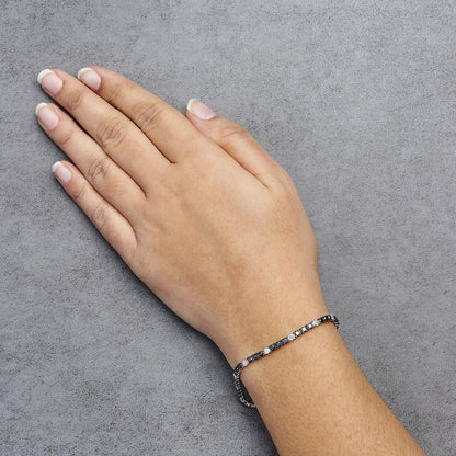 White metal bracelet with alternating black and white round gemstones in 4-prong settings, worn on a model's wrist, shown from above at an angle.