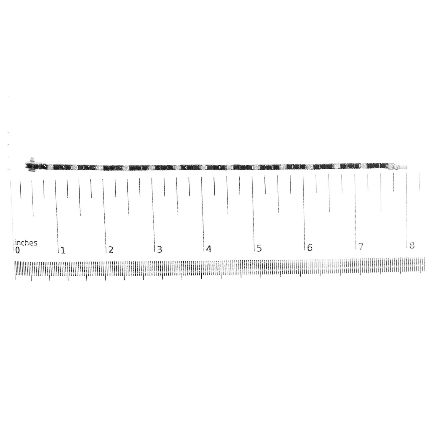 White metal bracelet set with alternating black and white round gemstones in 4-prong settings, laid flat on a ruler for size reference, shot from above.
