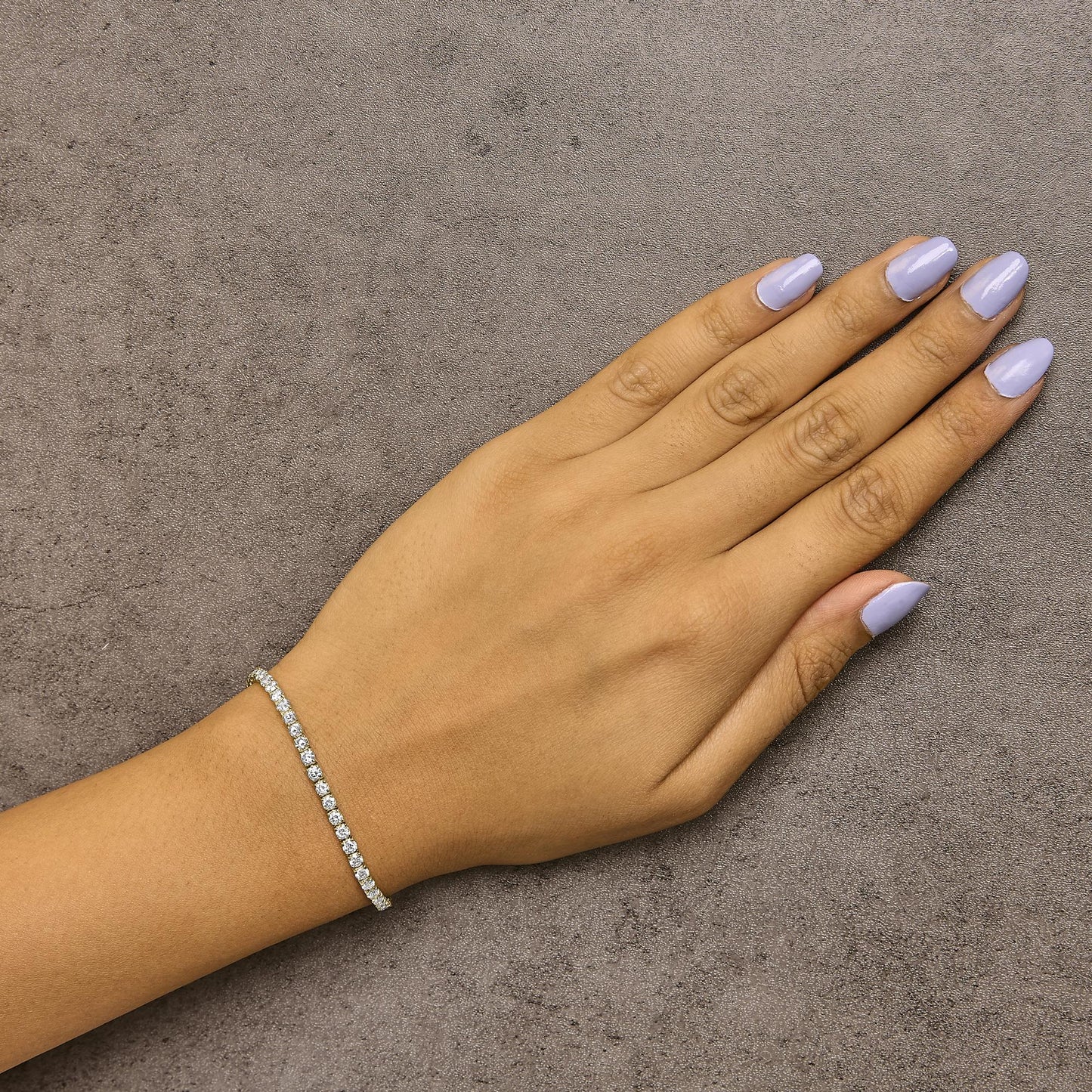 Yellow metal bracelet with round white gemstones in 4-prong settings, shown on a model's wrist from a top-down angle.