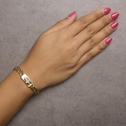 Close-up angled shot of a yellow bracelet with a rectangular plate featuring a cross embellished with round white gemstones, worn on a model's wrist.