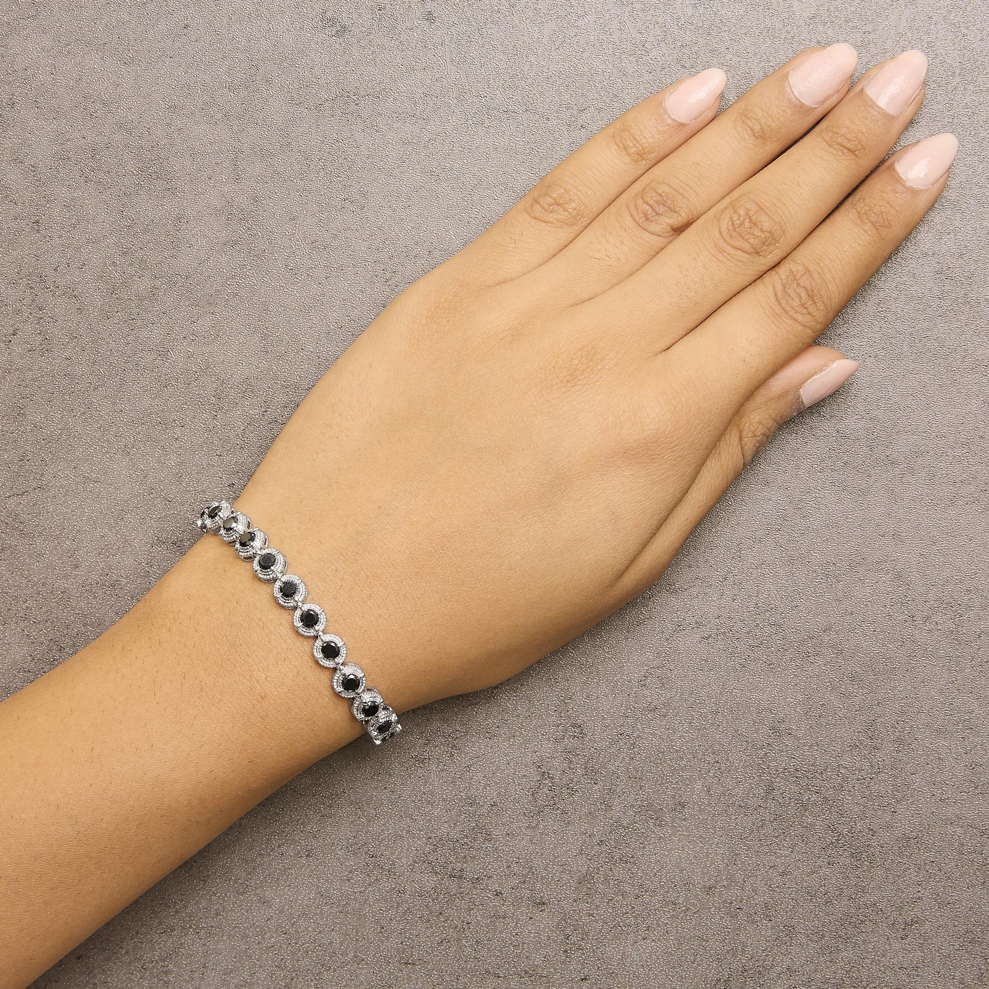 White metal bracelet with alternating round black gemstones in prong settings, shown worn on a model's wrist from a top-down angle.