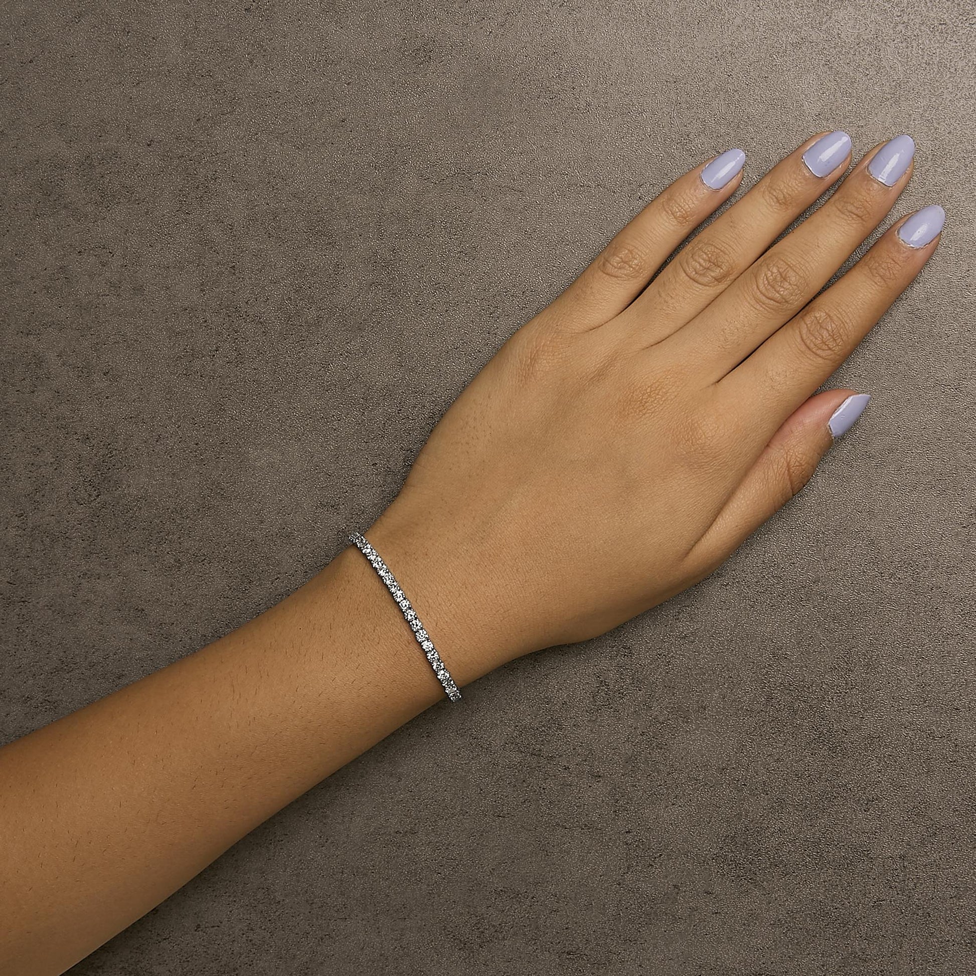 White metal bracelet with round white gemstones in 4-prong settings, worn on a model's wrist, shot from above.