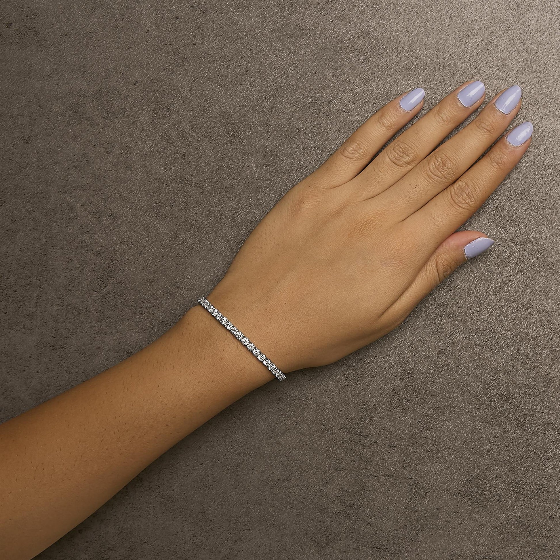 White metal bracelet with round white gemstones in prong settings, shown worn on a model's wrist, top-down angle.