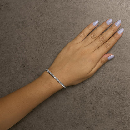 White metal bracelet with round white gemstones in prong settings, shown worn on a model's wrist, top-down angle.