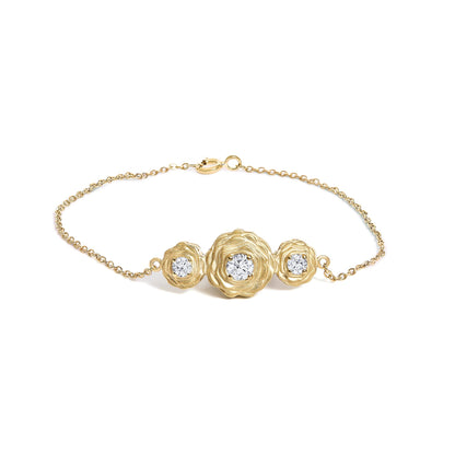 Yellow metal bracelet shown from the top on a white background, featuring three flower-shaped settings with round white gemstones in prong settings, one larger stone in the center and two smaller stones on each side.