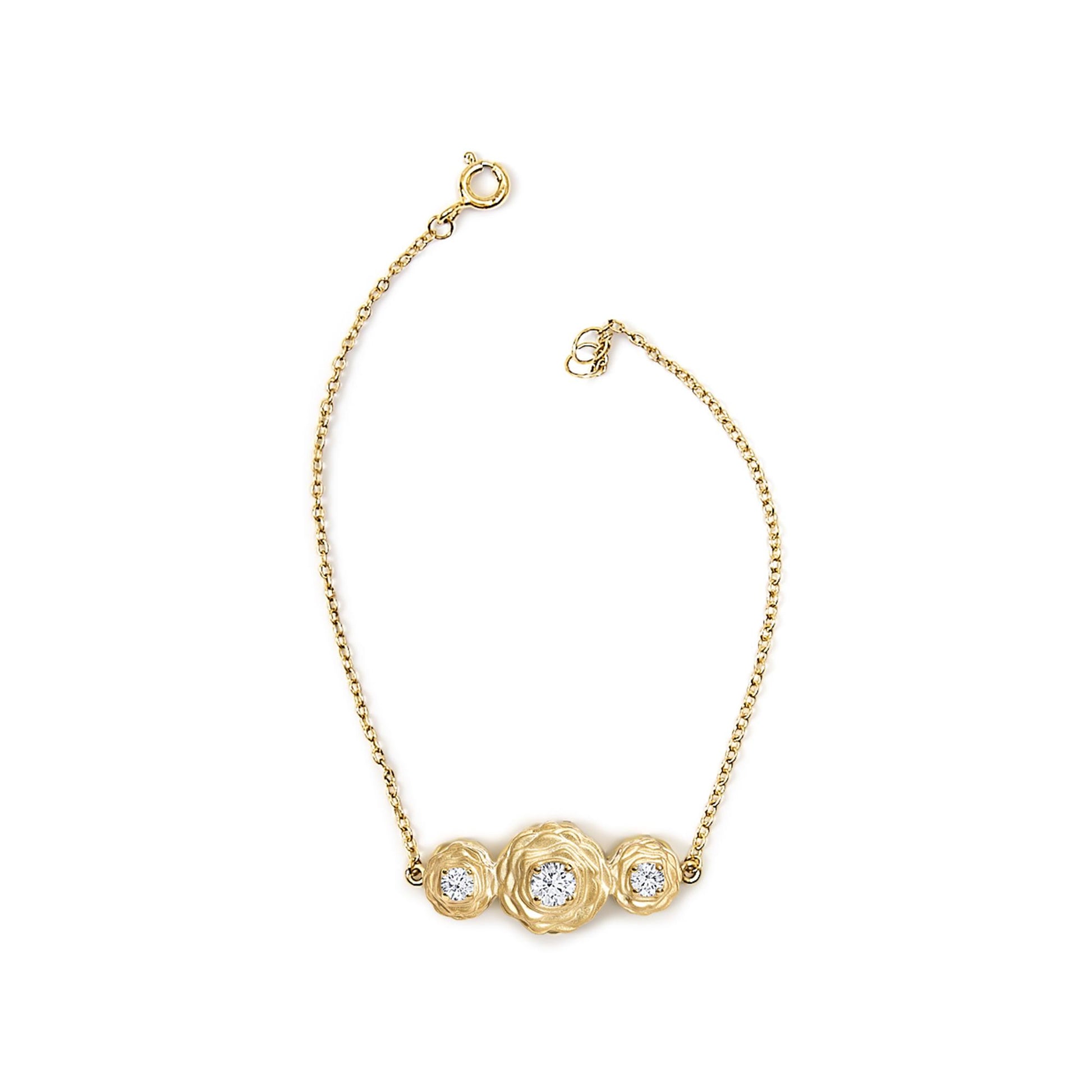 Yellow metal bracelet shown from above with a central cluster of three round white gemstones in prong settings.