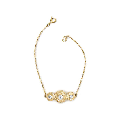 Yellow metal bracelet shown from above with a central cluster of three round white gemstones in prong settings.
