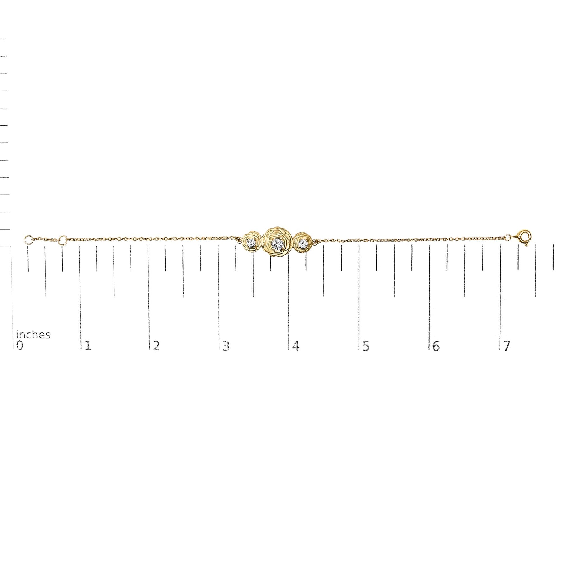 Yellow metal bracelet with three round white gemstones in prong settings arranged in a floral design, shown on a ruler scale from a top-down angle.