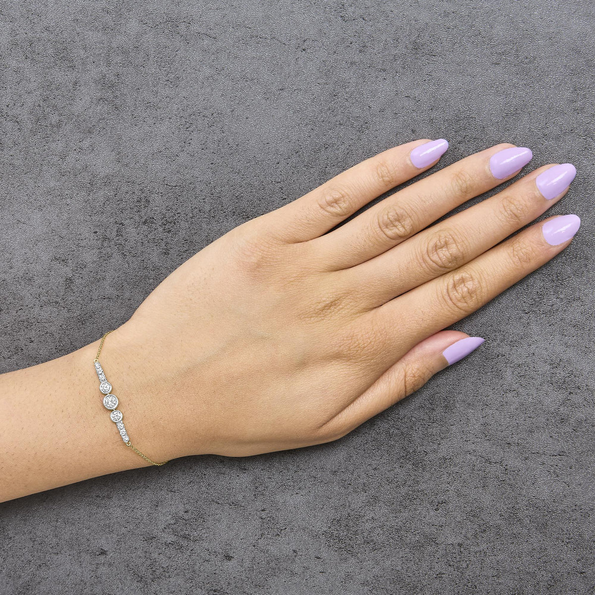 Yellow metal bracelet with multiple round white gemstones in prong settings, shown worn on a model's wrist, photographed from above.