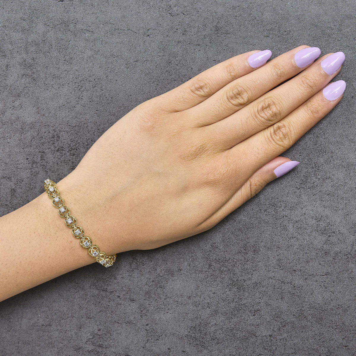 Close-up angled shot of a model's hand wearing a yellow metal bracelet adorned with round white gemstones in prong settings.