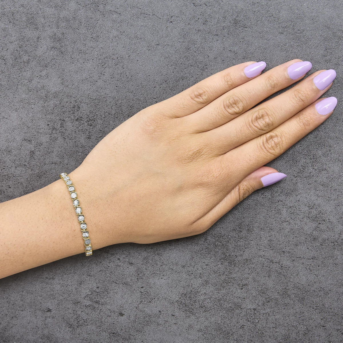 Yellow metal bracelet with round white gemstones in prong settings, shown worn on a model's wrist, angled top-down view.