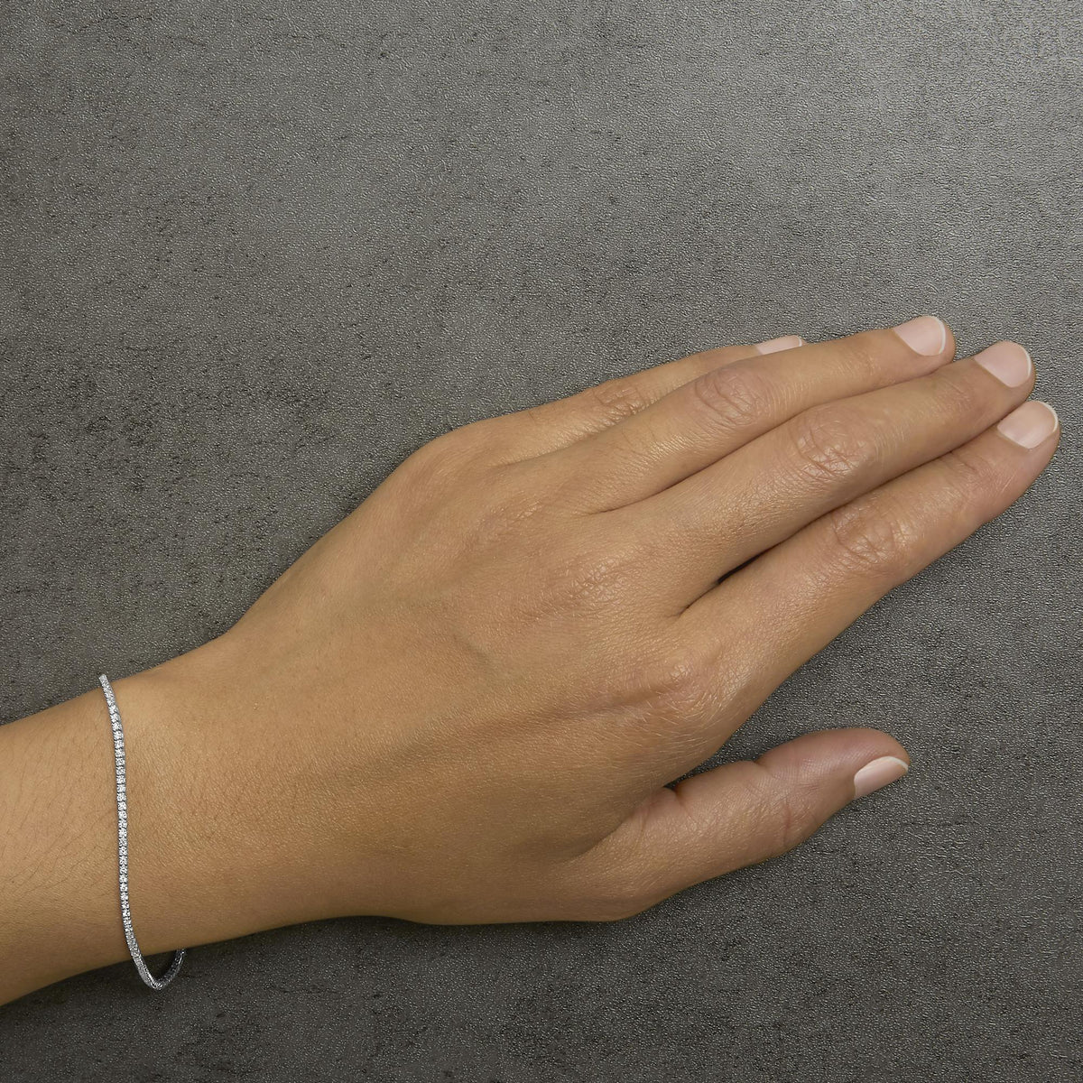 Bracelet with round white gemstones in prong settings shown worn on a model's wrist, top-down angle.