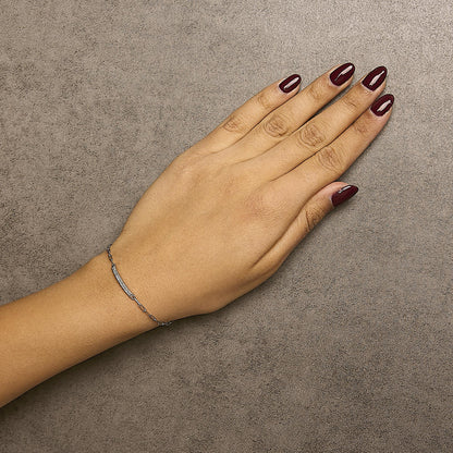 Bracelet with white metal chain and white round gemstones in prong setting, shown worn on a model's wrist, top-down angle.
