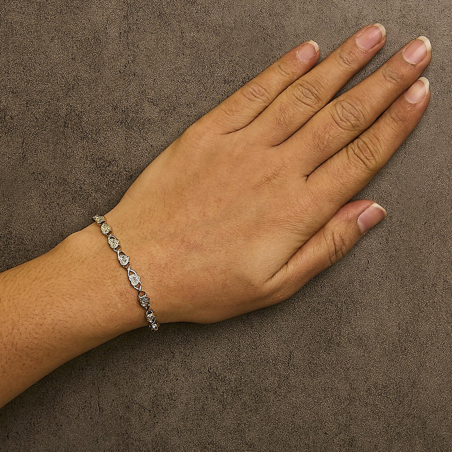 White metal bracelet with round white gemstones in prong settings, worn on model's wrist, shown from top angle.
