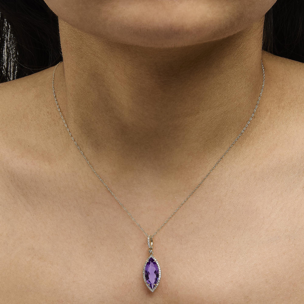 Yellow metal necklace with a marquise-shaped purple gemstone pendant surrounded by small round white gemstones in a micro-pave setting, shown worn on a model from a front angle.