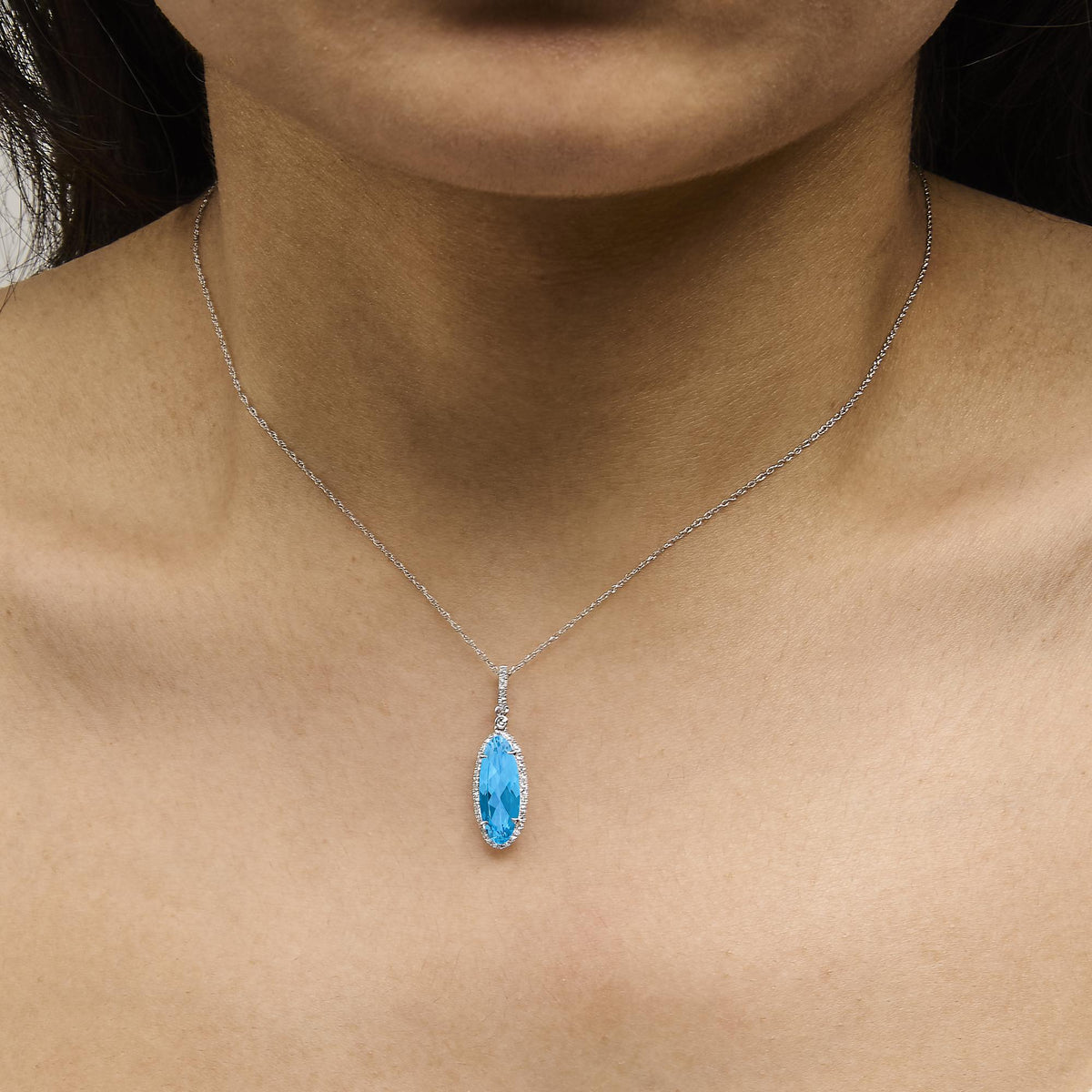 White metal necklace with a blue oval gemstone pendant surrounded by small white round gemstones in a micro-pave setting, shown worn on a model, front angle.