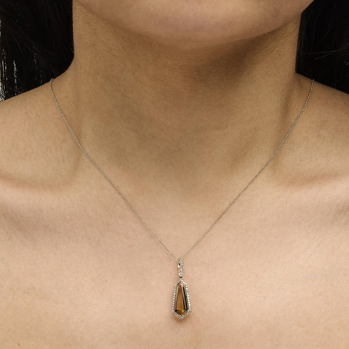Close-up front view of a 10K yellow gold shield-shaped citrine and 1/5 cttw diamond halo pendant necklace on a model
