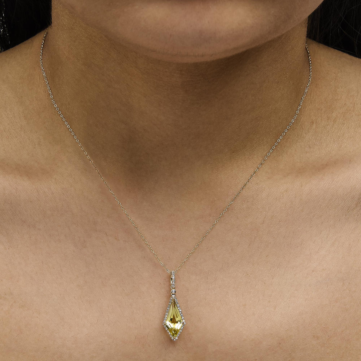 Close-up front view of a model wearing a yellow metal necklace with a lemon-colored gemstone pendant surrounded by small white gemstones in a micro-pave setting.