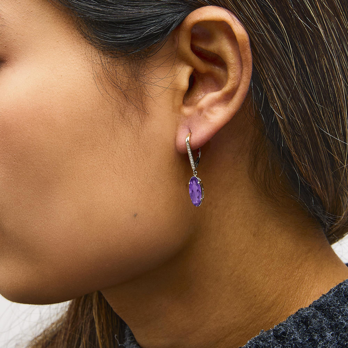 Close-up side view of 10K yellow gold leverback drop earrings showcasing an oval purple amethyst and diamond accents on a model