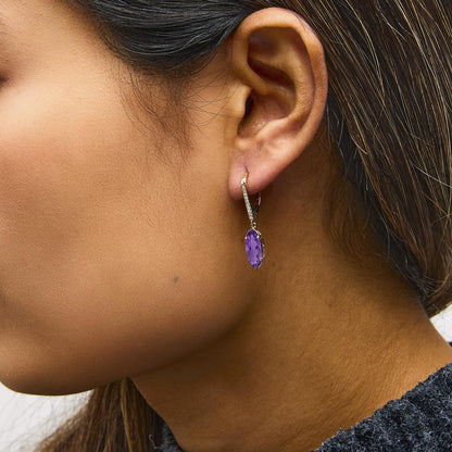 Close-up side view of 10K yellow gold leverback drop earrings showcasing an oval purple amethyst and diamond accents on a model