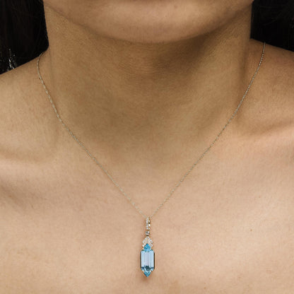 Yellow metal necklace with a rectangular blue gemstone pendant surrounded by small white gemstones in a micro-pave setting, shown worn on a model, close-up angle.
