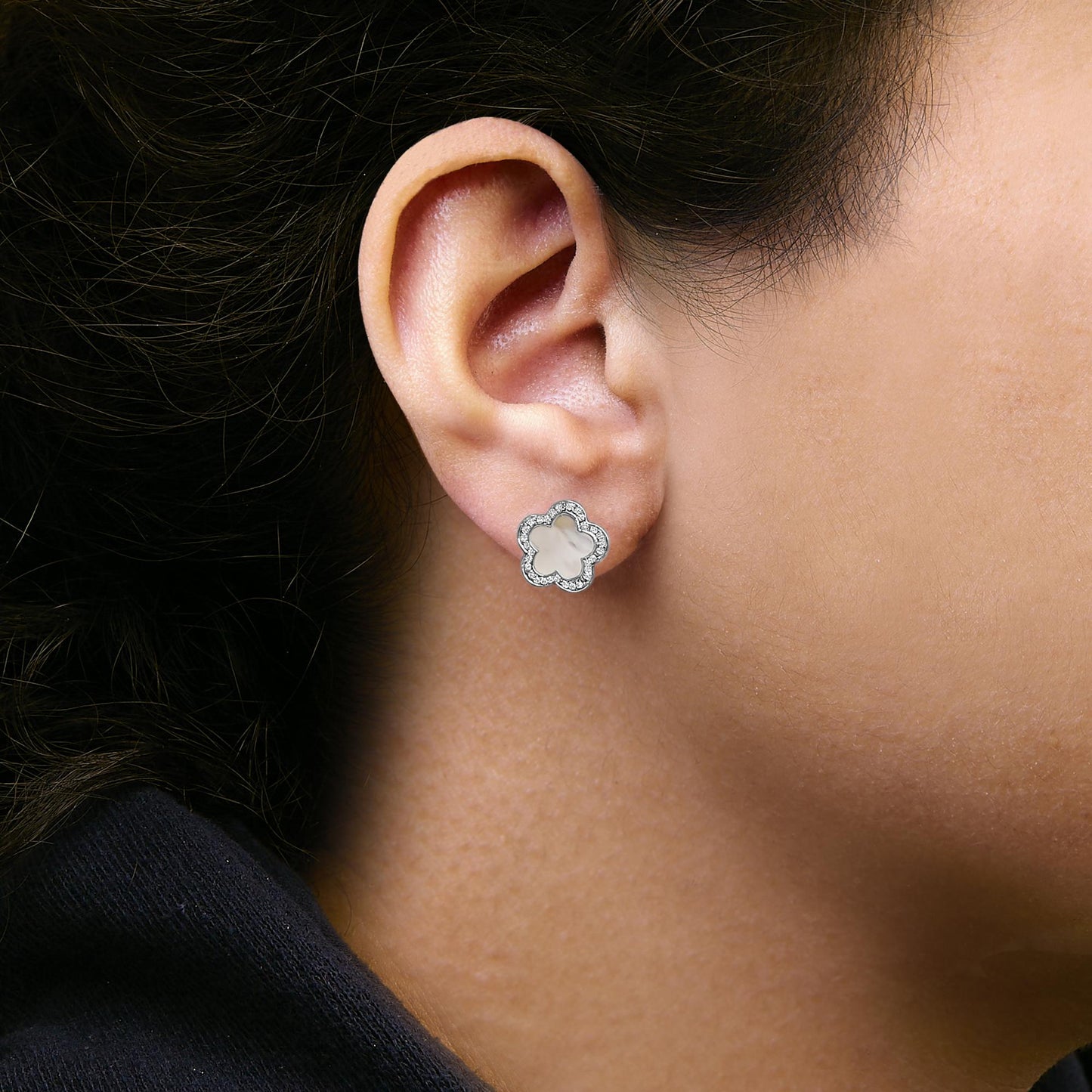 Close-up side view of a model wearing white metal stud earrings shaped like a five-petal flower with a white gemstone center and surrounded by small white gemstones in a micro-pave setting.