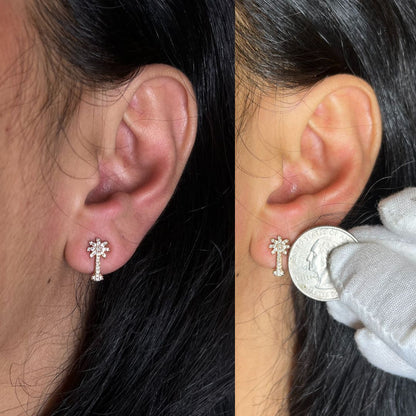 Rose metal earrings with a cluster of round white gemstones arranged in a floral pattern and a line of round white gemstones hanging below, shown on a model's ears from side angles. One image includes a quarter held next to the earring for size reference.