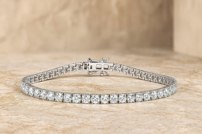 White metal tennis bracelet with two rows of round white gemstones in 4-prong settings, shown flat on a textured beige surface, front angle.