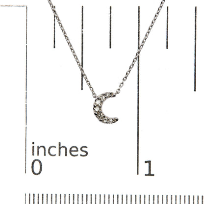 Close-up front view of a white metal necklace with a crescent moon pendant featuring multiple round white gemstones in pave settings, displayed on a ruler for size reference.