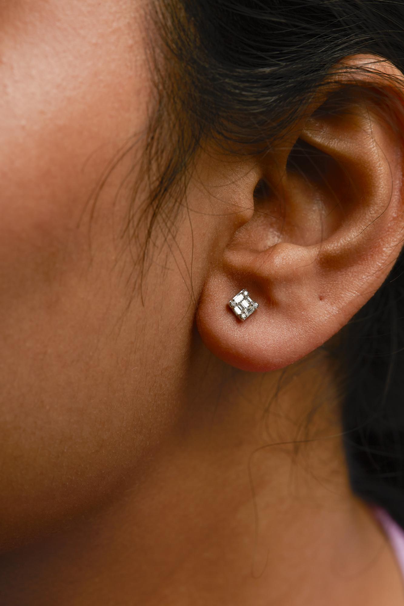 Close-up side view of a white metal stud earring on a model's ear, featuring multiple small rectangular and round white gemstones in different settings.