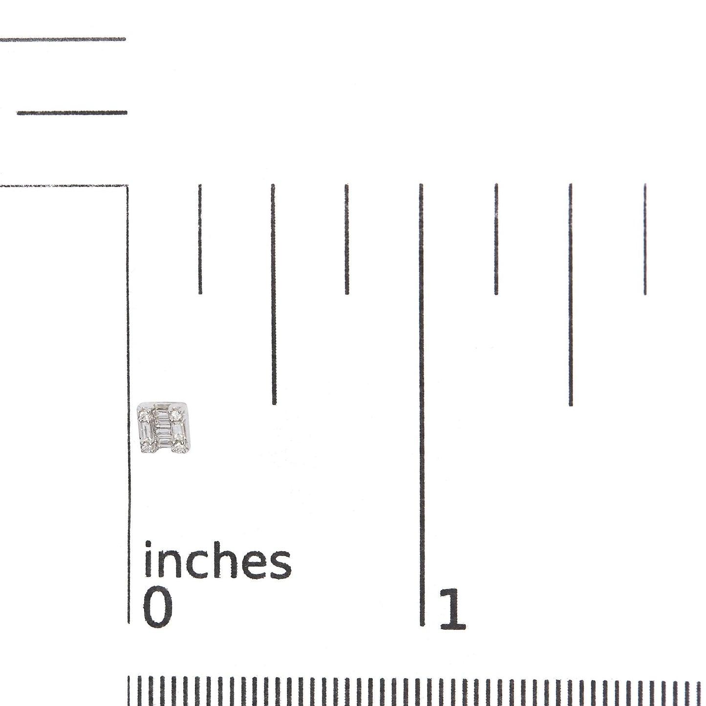 Close-up front view of a white metal earring with a geometric design featuring baguette and round white gemstones, shown on a ruler for size reference.