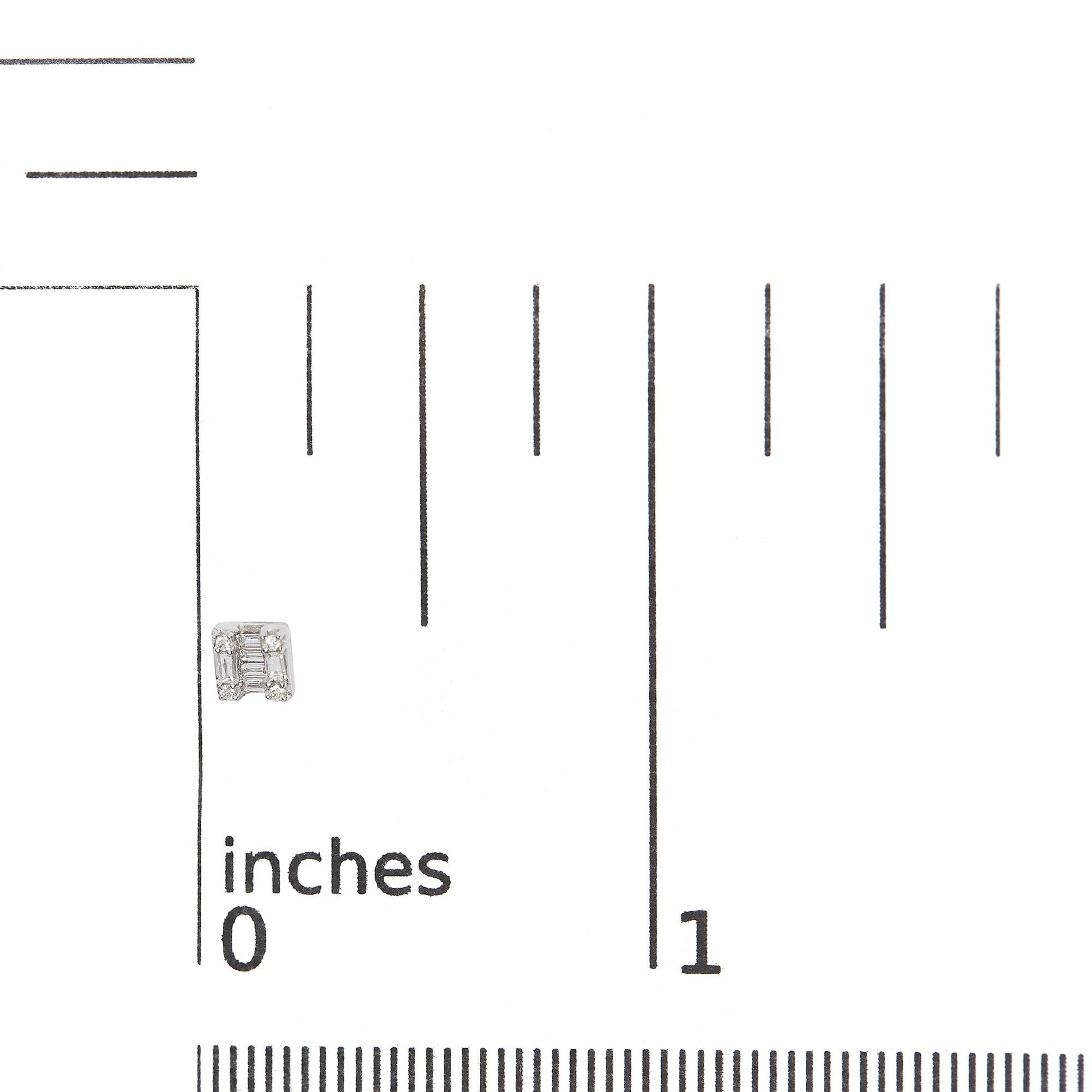 Close-up front view of a white metal earring with a geometric design featuring baguette and round white gemstones, shown on a ruler for size reference.