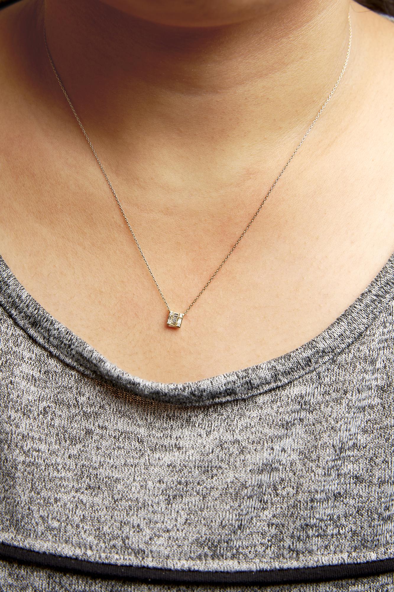 Close-up front view of a yellow metal necklace on a model featuring a small pendant with white gemstones in round and baguette shapes in prong and channel settings.